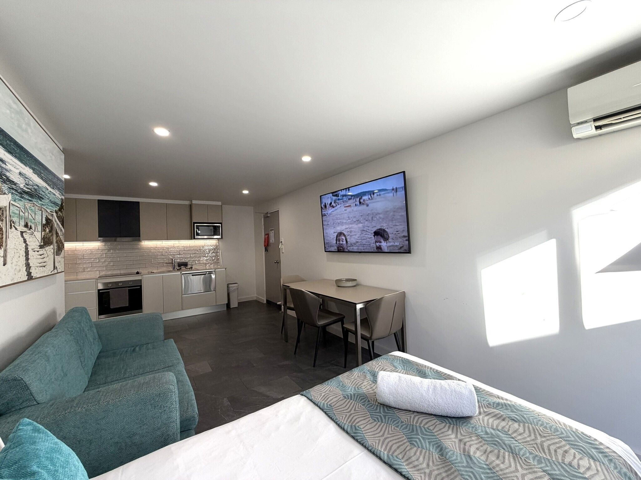 A compact living space with a kitchenette, a dining area, a sofa, and a bed with a patterned blanket.