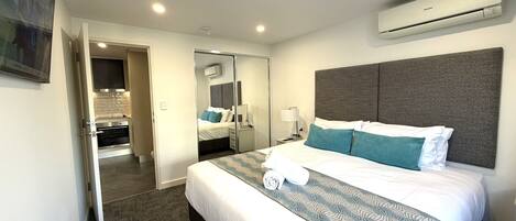 Une chambre d’hôtel comprenant un lit, un miroir, un climatiseur, une table de chevet et une porte donnant accès à une salle de bain.