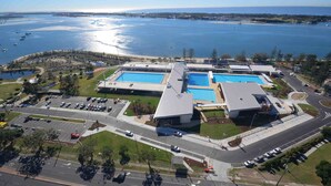 An aerial view of a complex with multiple swimming pools, parking areas, and a road leading to the complex. - Southport Motel & Apartments (Southport)