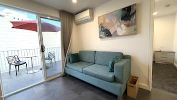 Una sala de estar moderna con un sofá gris, un ventanal que da a un área exterior con un paraguas rojo, y un cuadro en la pared.