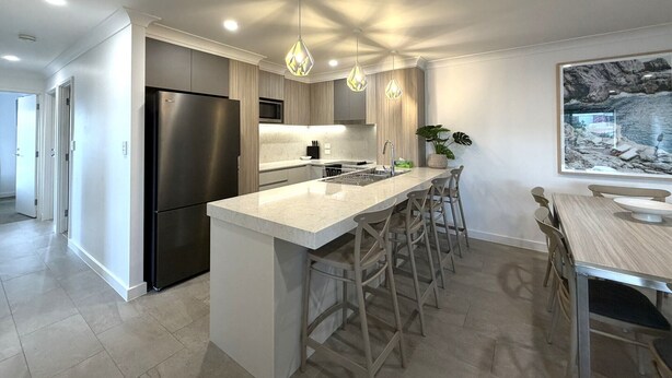 A modern kitchen with a central island, bar stools, and pendant lighting. - Southport Motel & Apartments (Southport)
