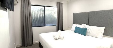 Quarto de hotel com cama, cortinas, ventilador de teto e televisão fixada na parede.