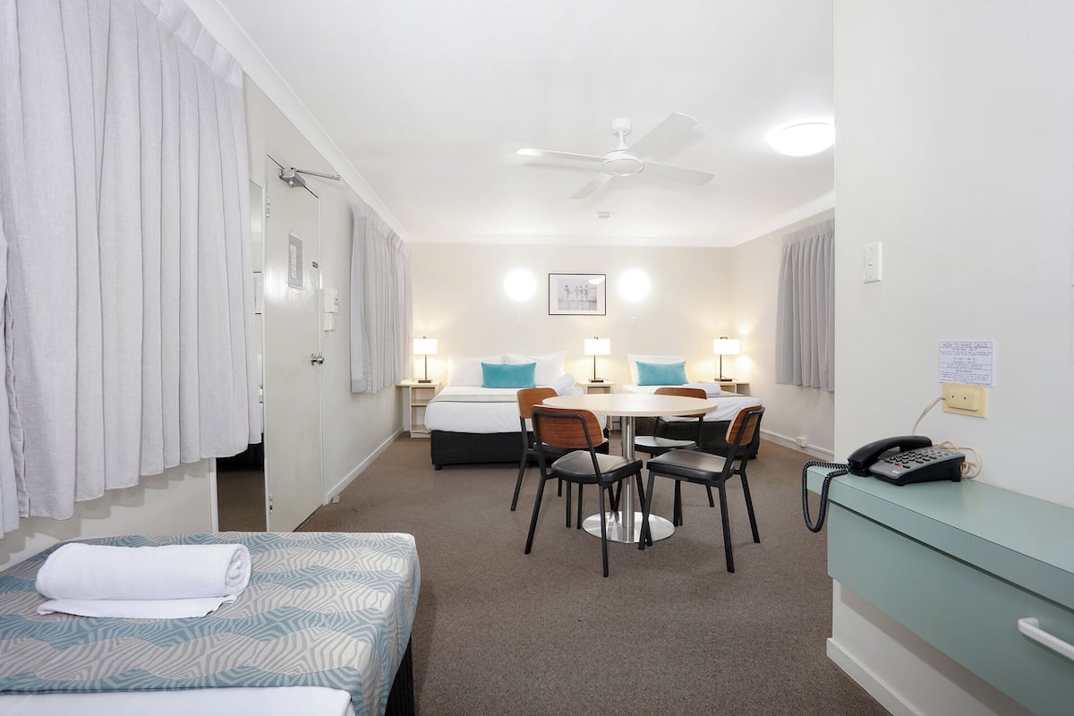 A hotel room with a bed, a desk, a chair, a phone, and a ceiling fan.