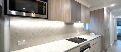 A modern kitchen with a built-in microwave, stove, and oven, light wood cabinetry, and a marble countertop.