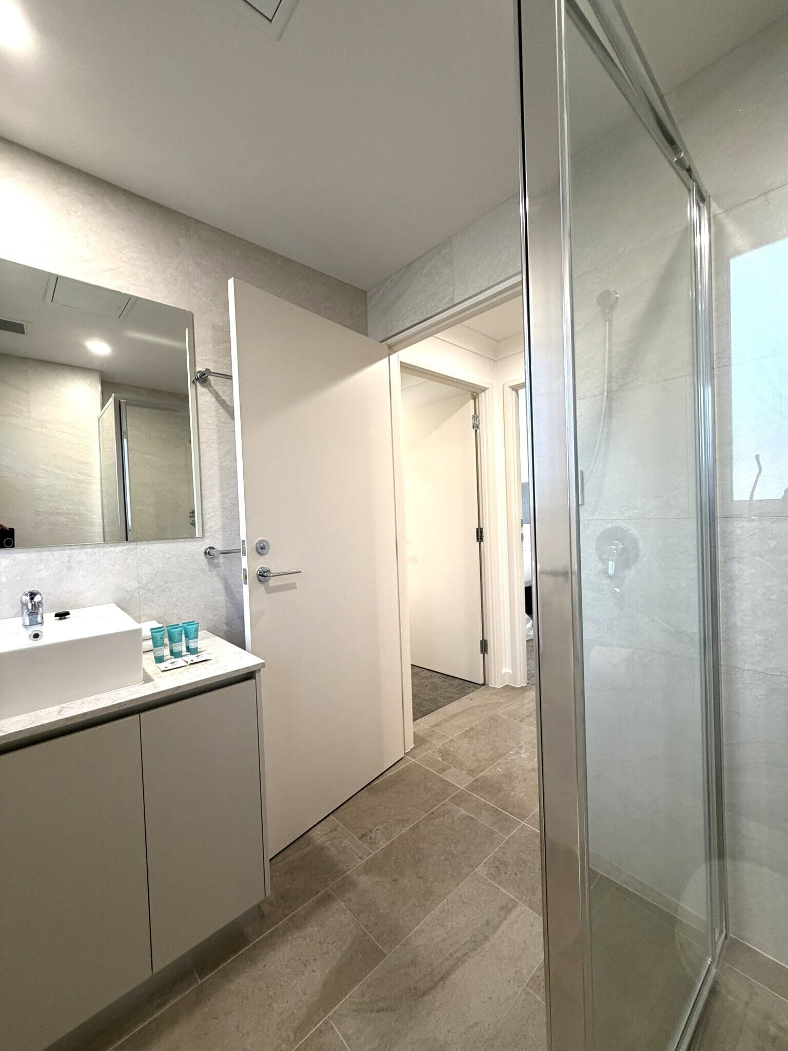 Un baño moderno con cabina de ducha de vidrio, un lavamanos blanco y un espejo.