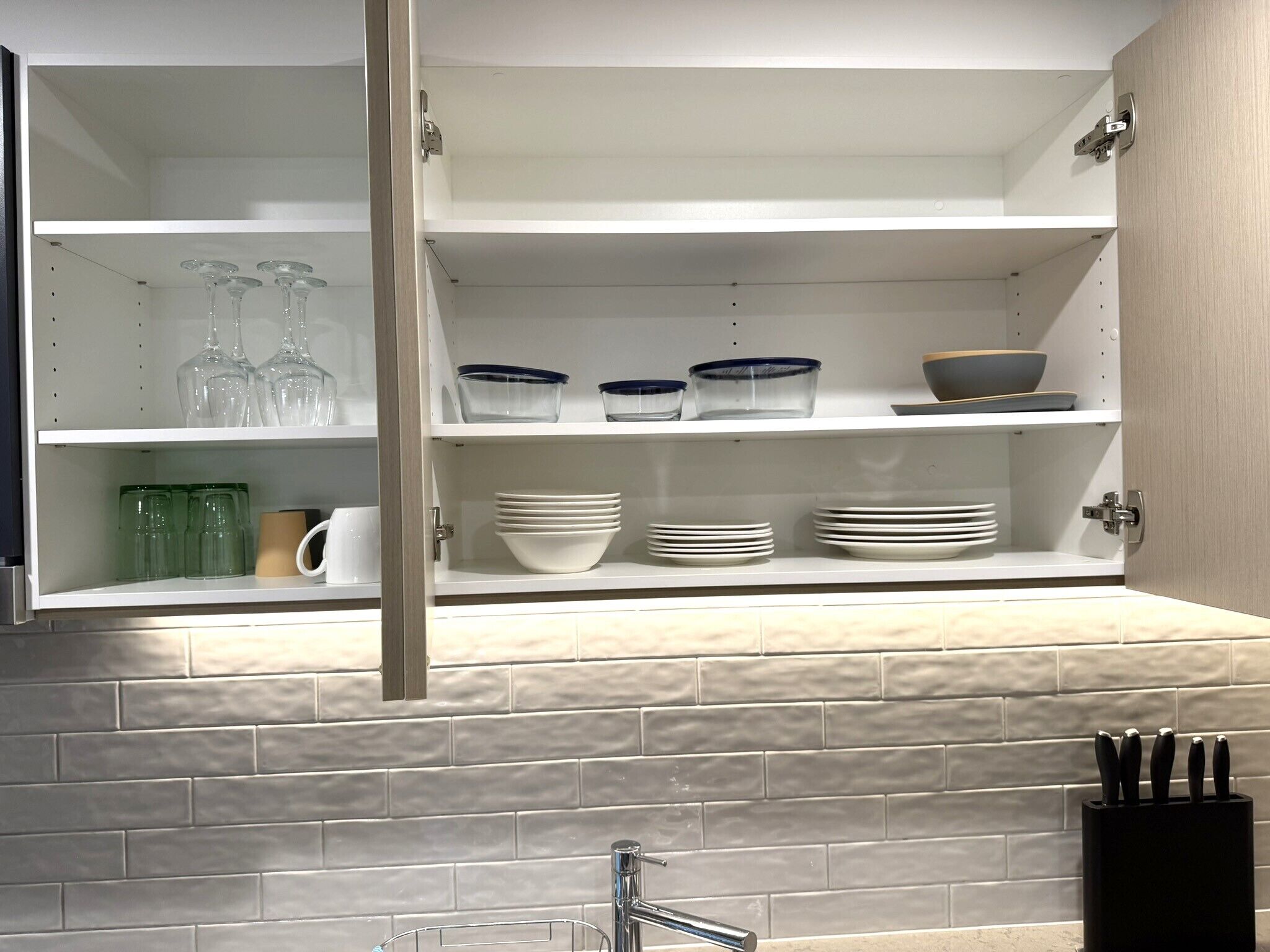 A kitchen with white cabinets, a tiled backsplash, and a knife block.