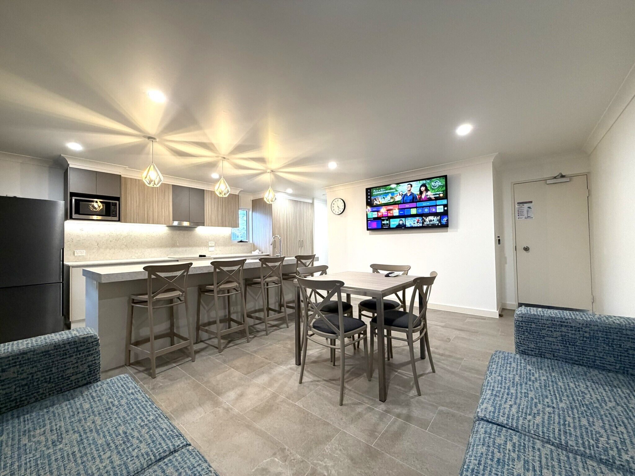Una cocina moderna con una isla central, taburetes de bar, una mesa de comedor y un televisor de pantalla plana montado en la pared.