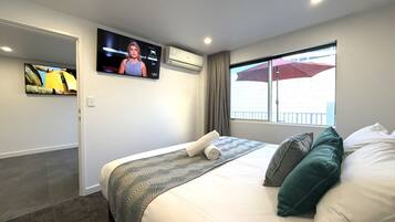 A hotel room with a bed, a TV mounted on the wall, a window with an umbrella, and a door.
