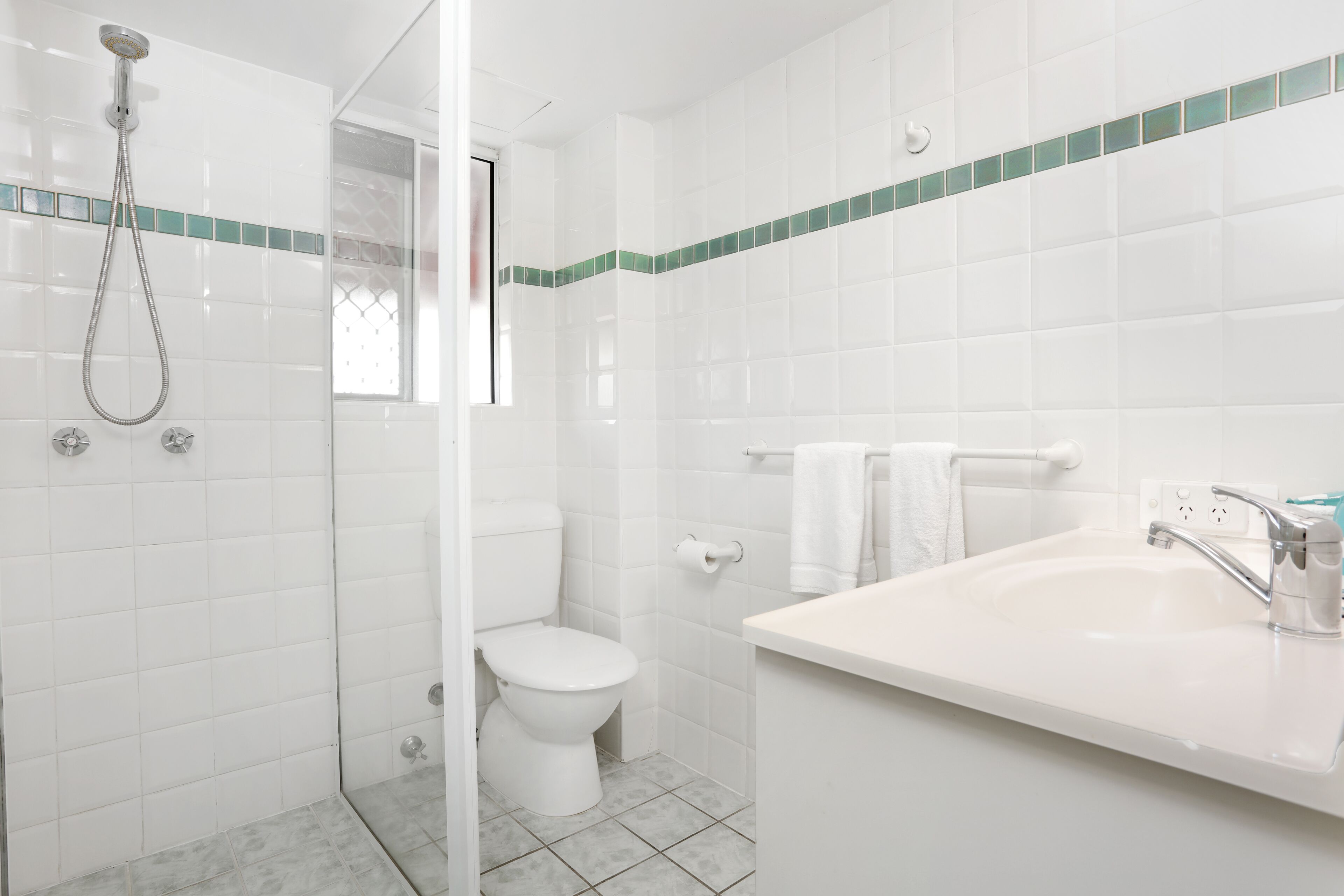 A bathroom with white tiles, a shower, a toilet, and a sink with a mirror.