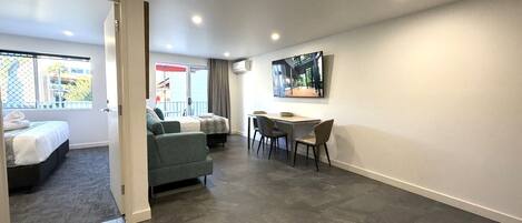 Una habitación de hotel moderna con cama, sofá, mesa de comedor con sillas y un gran ventanal.