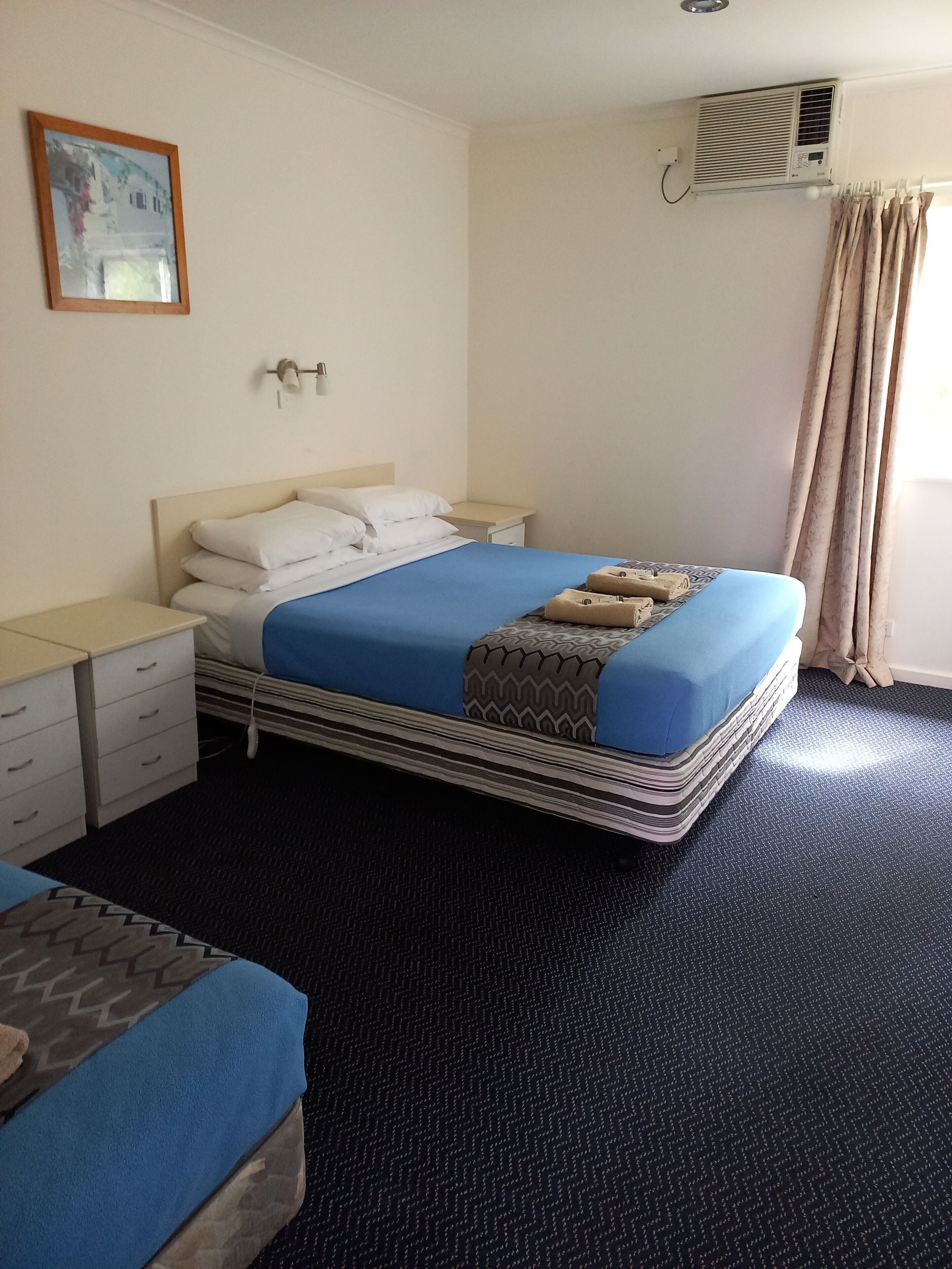 A hotel room with a bed, bedside table, and a small desk.