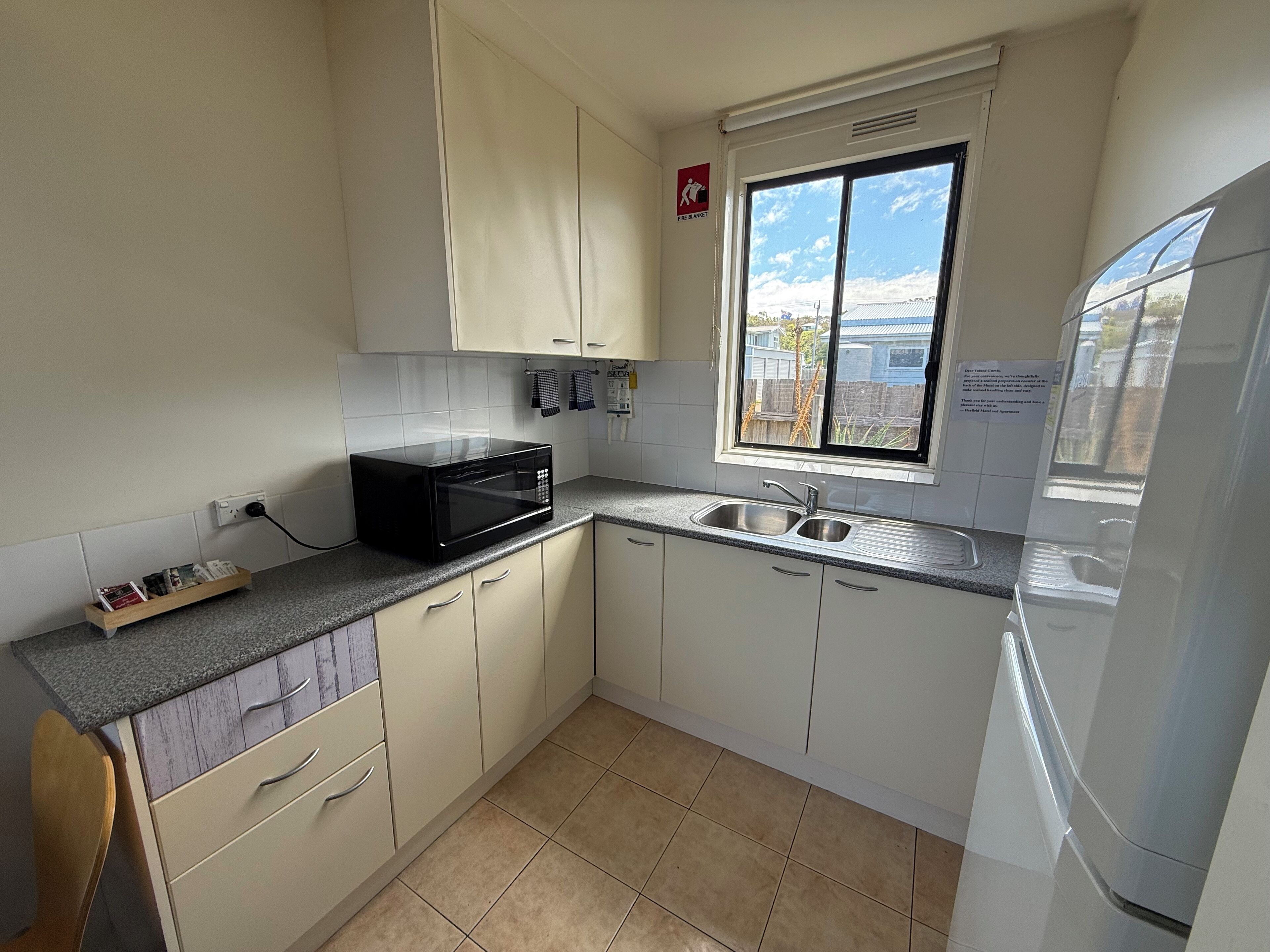 A compact kitchen with white cabinets, a black microwave, a stainless steel sink, and a window with a view of the outside.