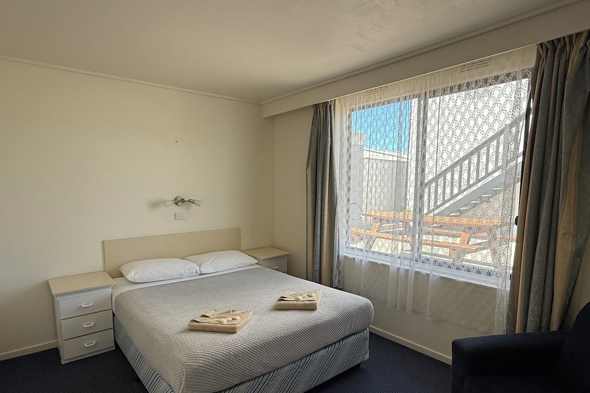 A hotel room with a bed, bedside tables, a chair, and a window with curtains.