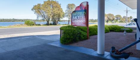 A sign for Heyfield Motel & Apartments with a view of a lake and trees in the background.