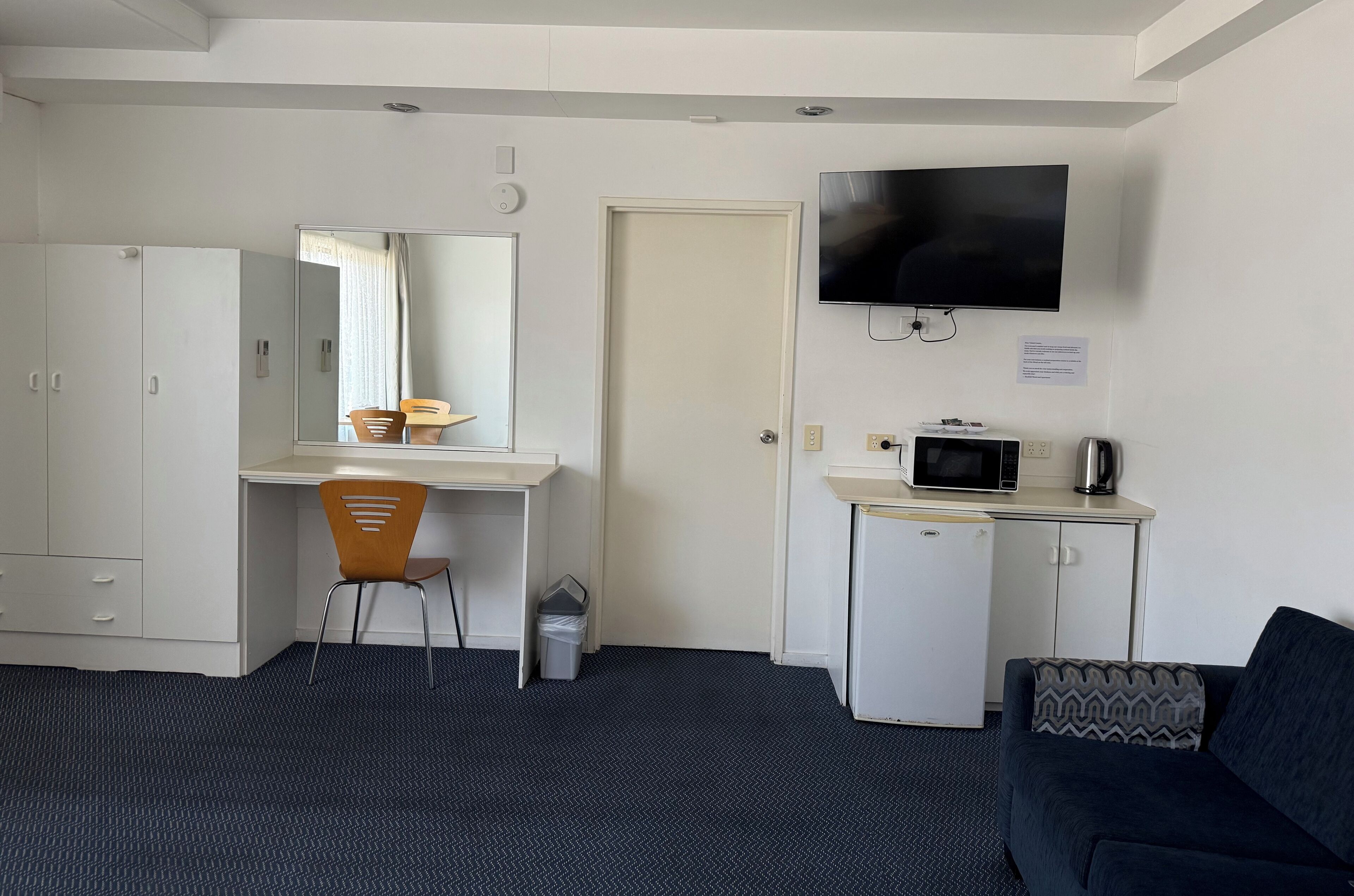 Habitación con escritorio, silla, televisión, microondas y un refrigerador pequeño.