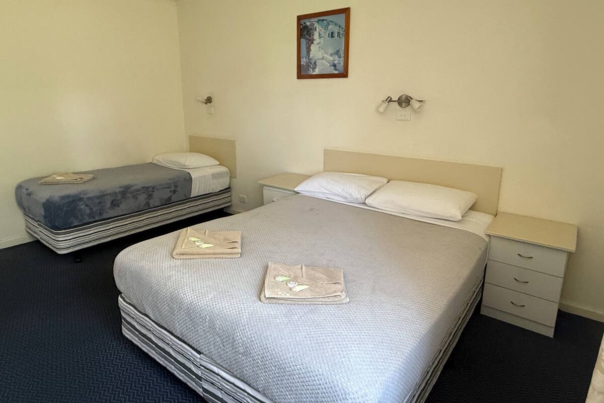 A hotel room with a large bed, a smaller bed, a nightstand, a drawer unit, and a painting on the wall.