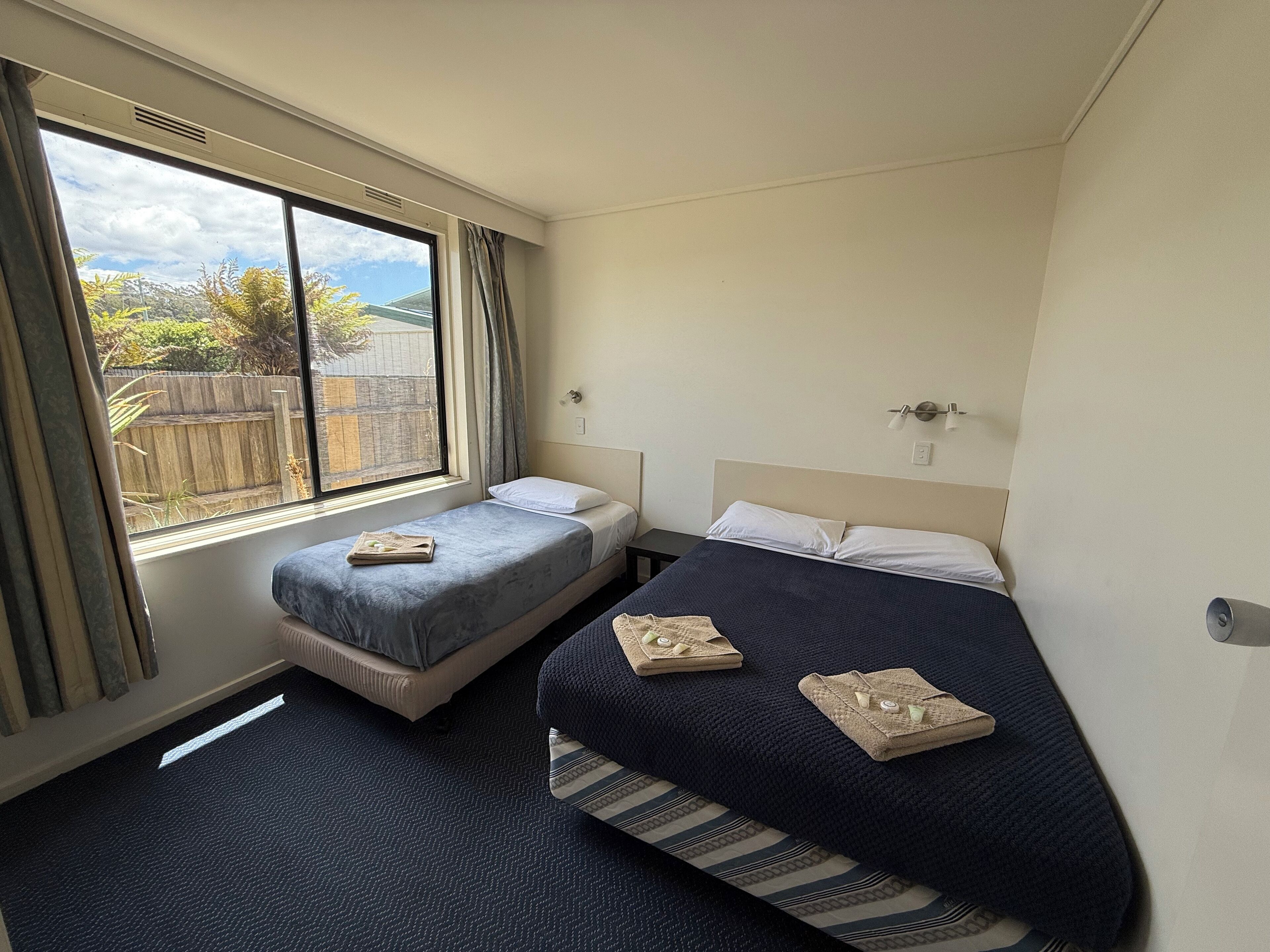 A hotel room with two beds, a window with curtains, a radiator, and a view of the outside.