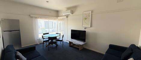 Camera d'albergo compatta con divano, tavolo da pranzo con sedie, televisore e frigorifero.