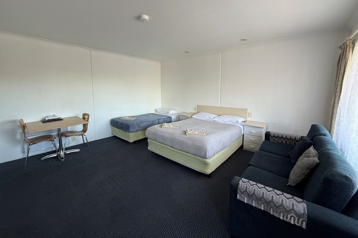 A hotel room with a bed, a desk, a chair, a sofa, and a window with curtains.