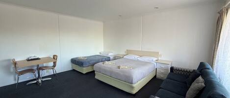 A hotel room with a bed, a desk, a chair, a sofa, and a window with curtains.