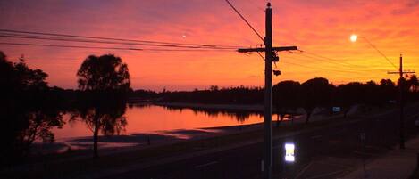 A sunset over a calm body of water with a street and utility poles in the foreground.
