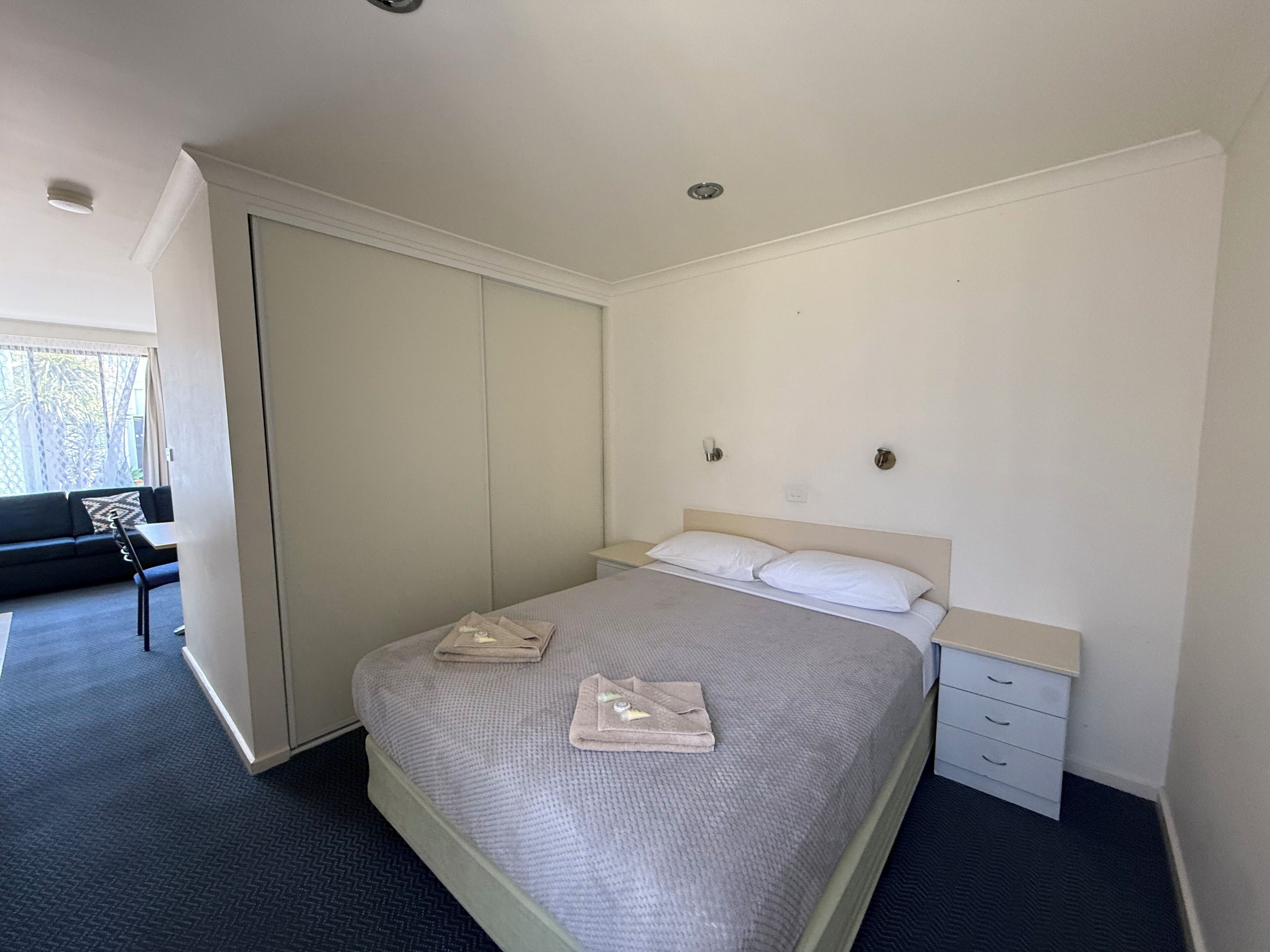 A bedroom with a bed, a nightstand, a wardrobe, and a seating area with a sofa and a table.