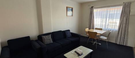 Una sala de estar con un sofá de color oscuro, una mesita de centro y una mesa de comedor con sillas.