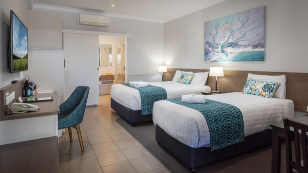 A hotel room with two beds, a desk, a chair, and a painting on the wall.