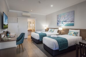 A hotel room with two beds, a desk, a chair, and a painting on the wall.
