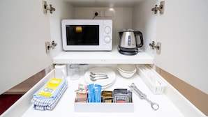 A kitchen area with a microwave, kettle, and various kitchen utensils and food items.