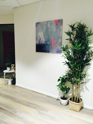 Ein Zimmer mit einem großen, abstrakten Gemälde an der Wand, einer hohen Bambuspflanze und einem kleinen Tisch mit Topfpflanzen.