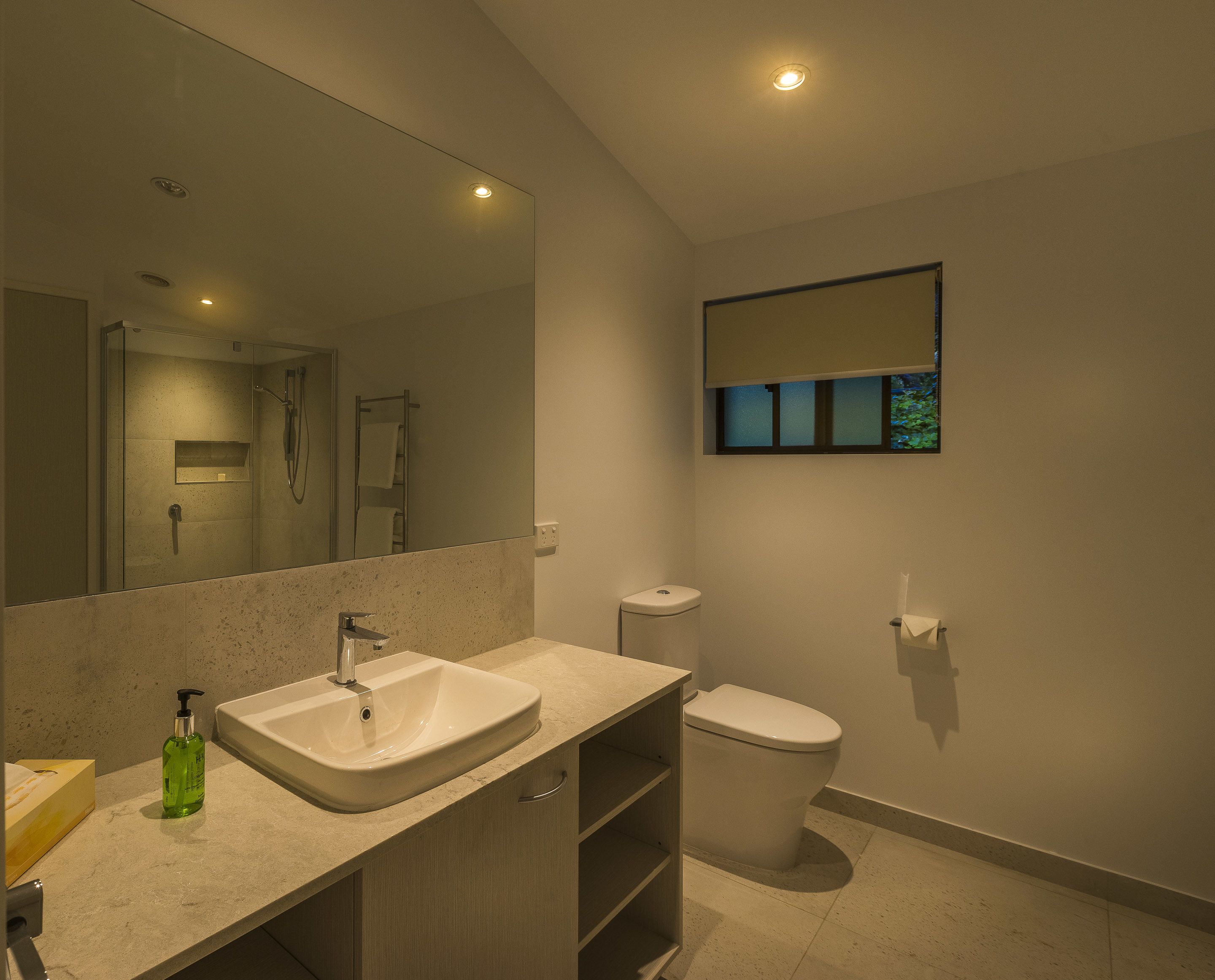 Une salle de bain moderne avec un grand miroir, un lavabo, des toilettes et une petite fenêtre.