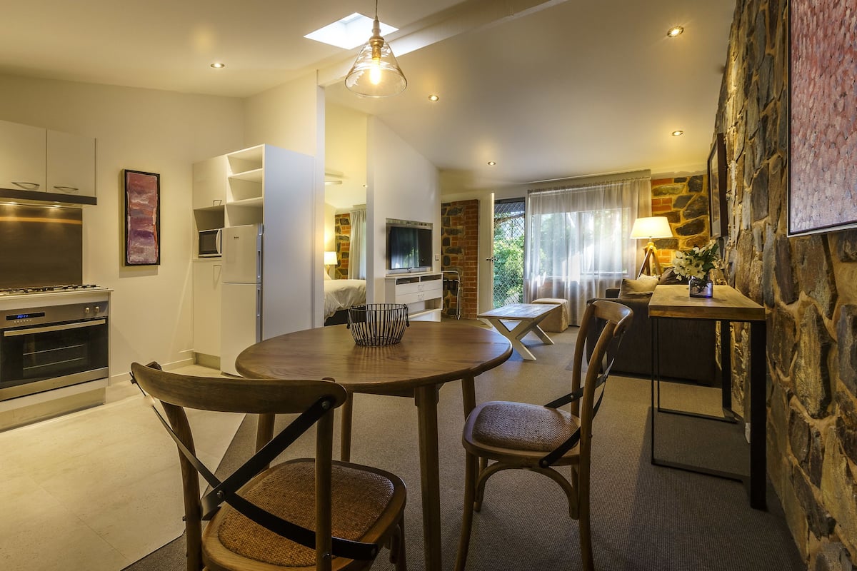 A modern kitchen with a built-in oven, a dining area with a round table and chairs, and a stone accent wall.