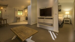 A modern hotel room with a flat-screen TV, a dining table, a kitchen area, and a bed with a nightstand. - Bright Mystic Valley (Bright)