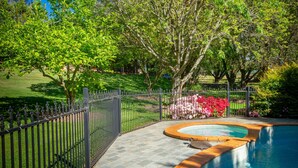 A swimming pool with a stone border, surrounded by a fenced garden area with trees and flowering plants. - Bright Mystic Valley (Bright)