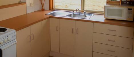 A kitchen with wooden cabinets, a sink, a microwave, and a window with a view.
