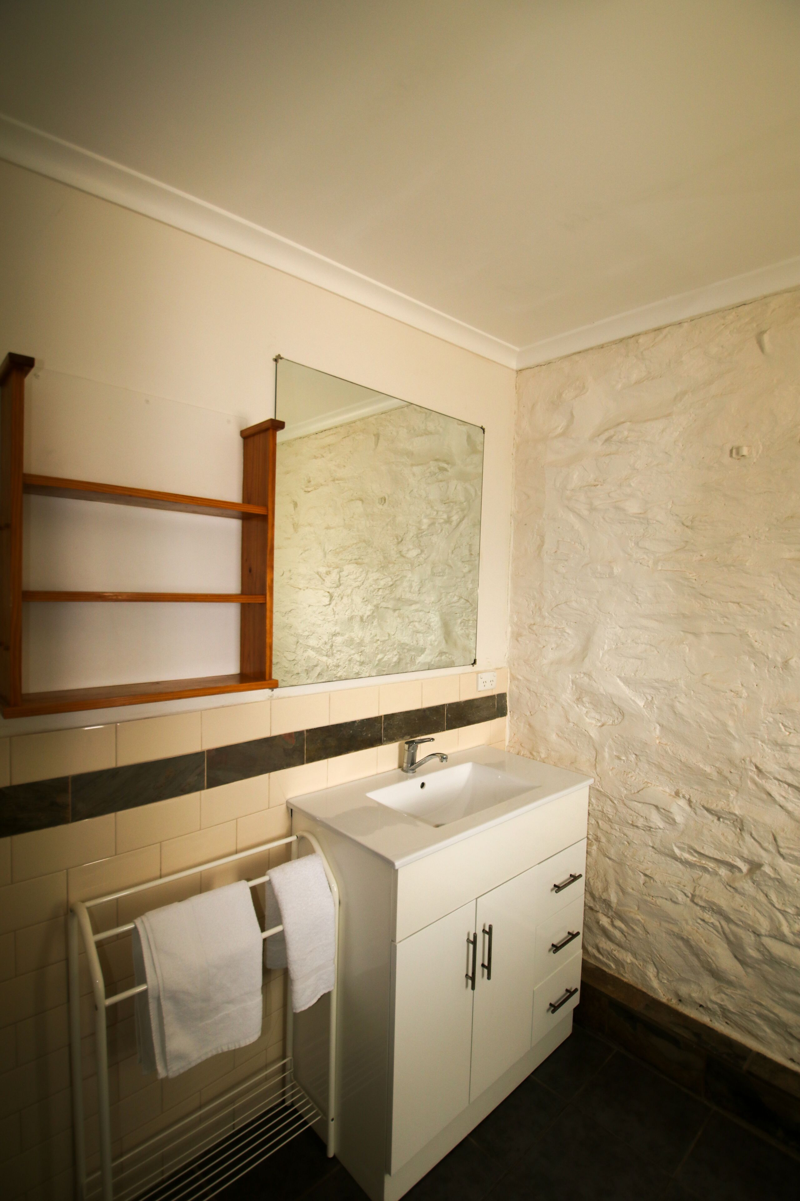 Un baño con tocador blanco, espejo, toallero y pared con textura.