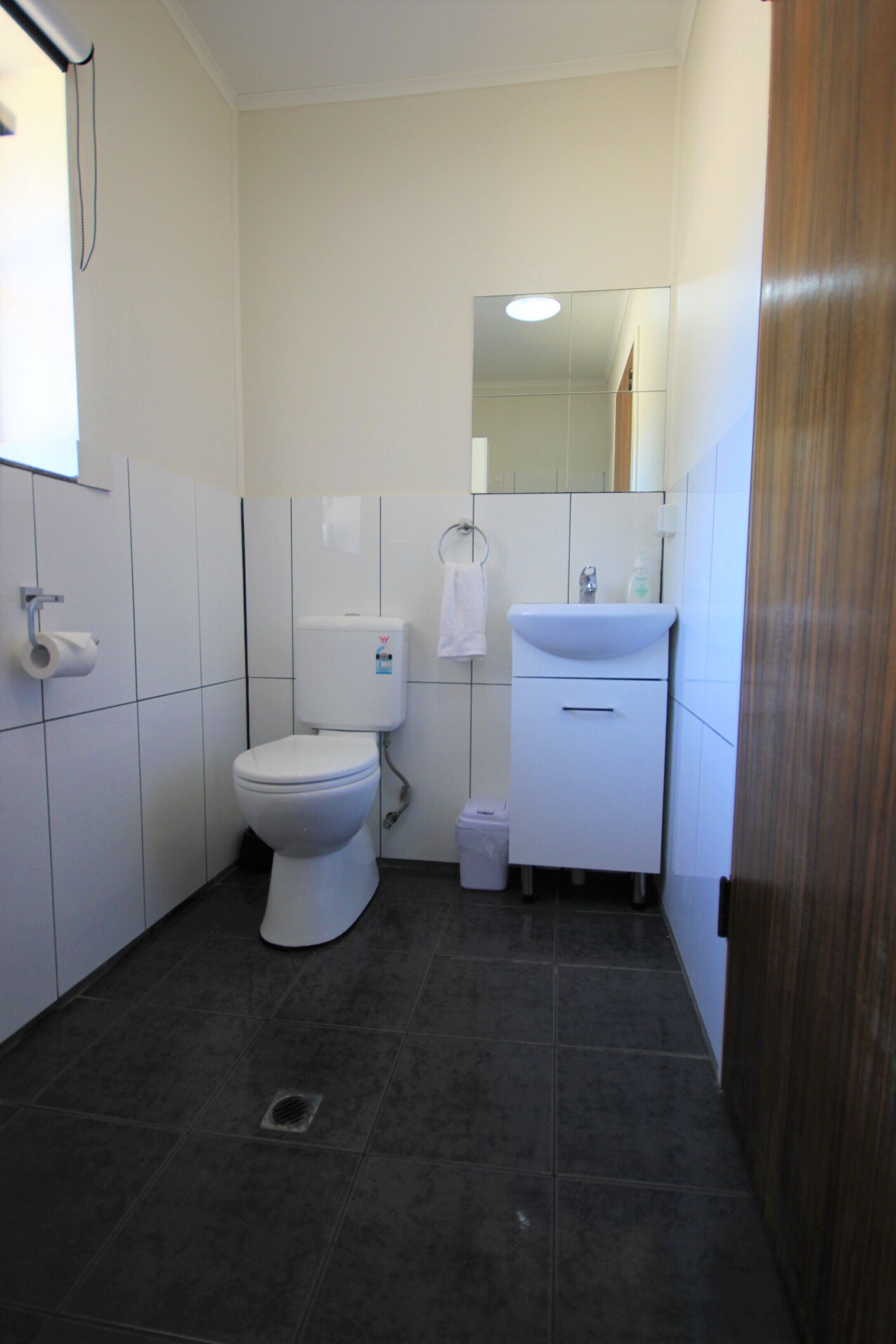 A small, clean bathroom with a toilet, sink, and mirror.