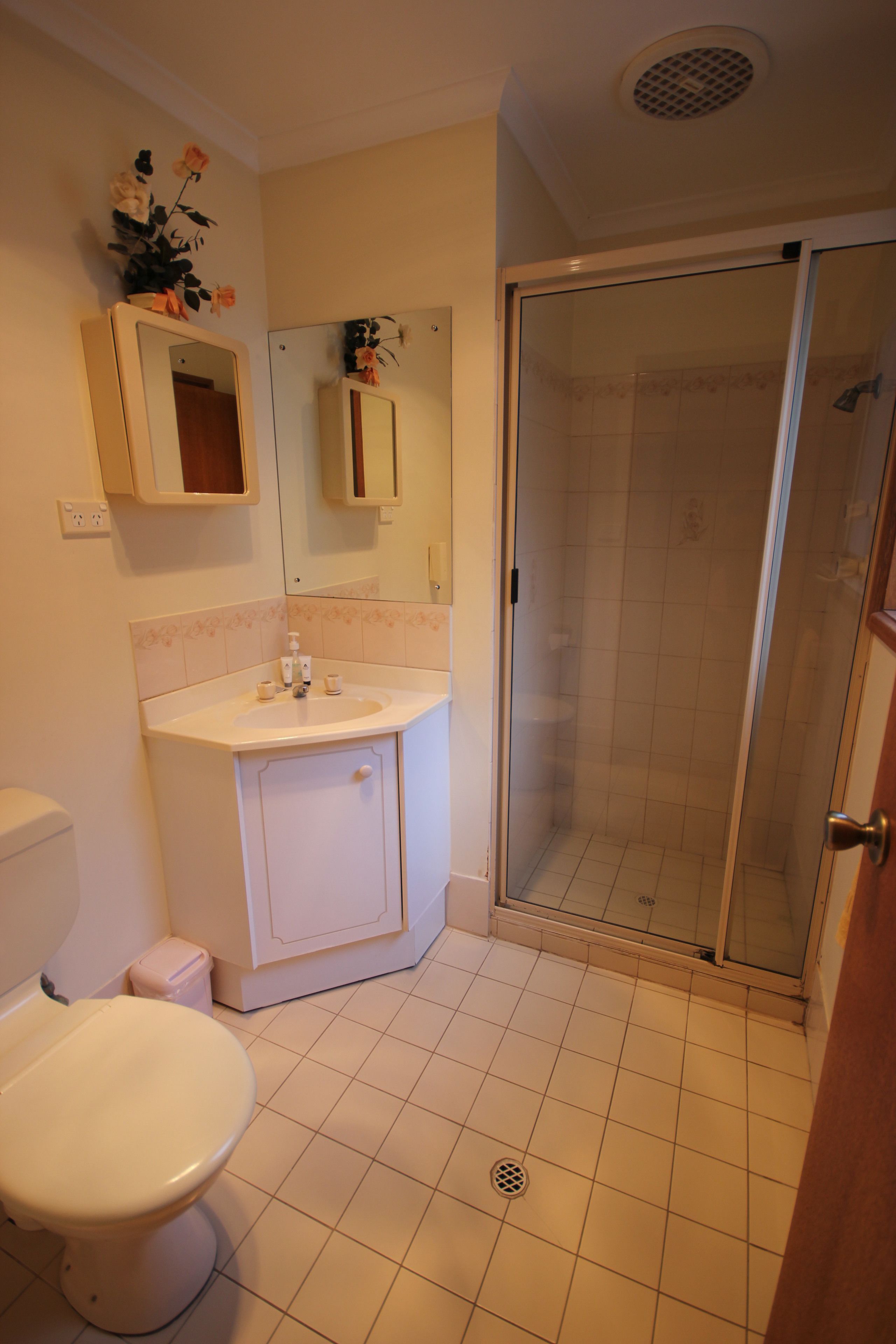 A bathroom with a toilet, sink, mirror, and shower.
