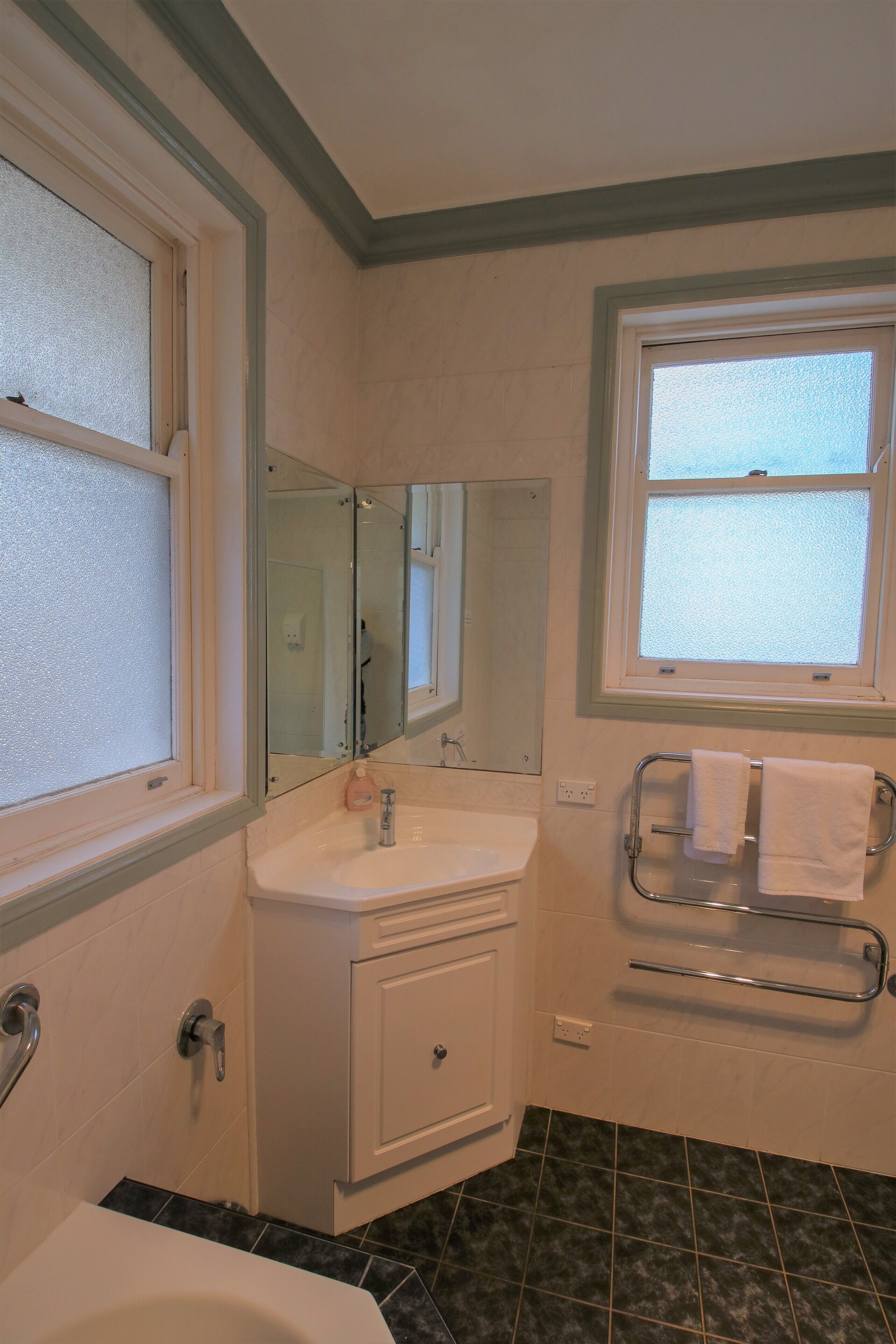 A bathroom with a white sink, a mirror, a window, and a shower area.