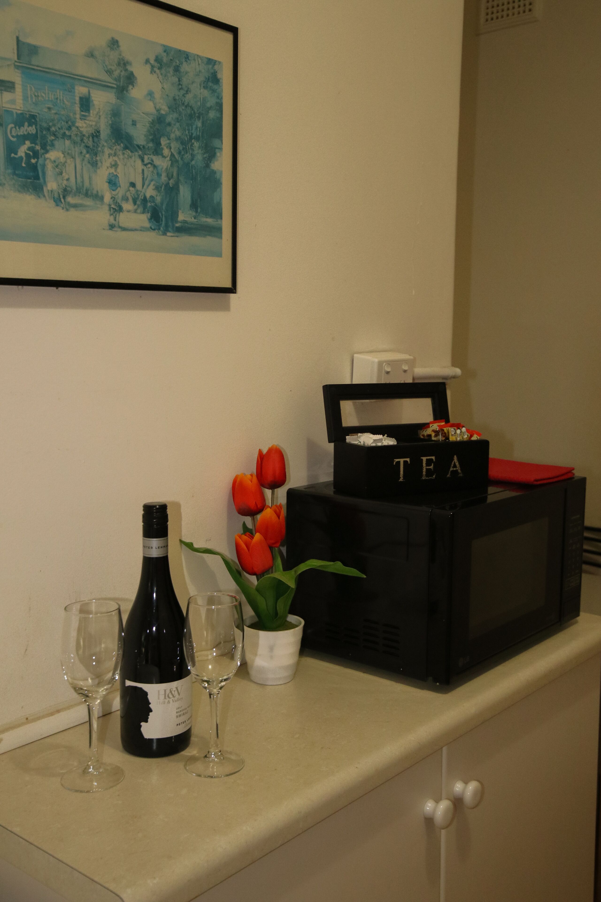 A kitchen counter with a wine bottle, two glasses, a potted plant, and a box labeled "TEA".