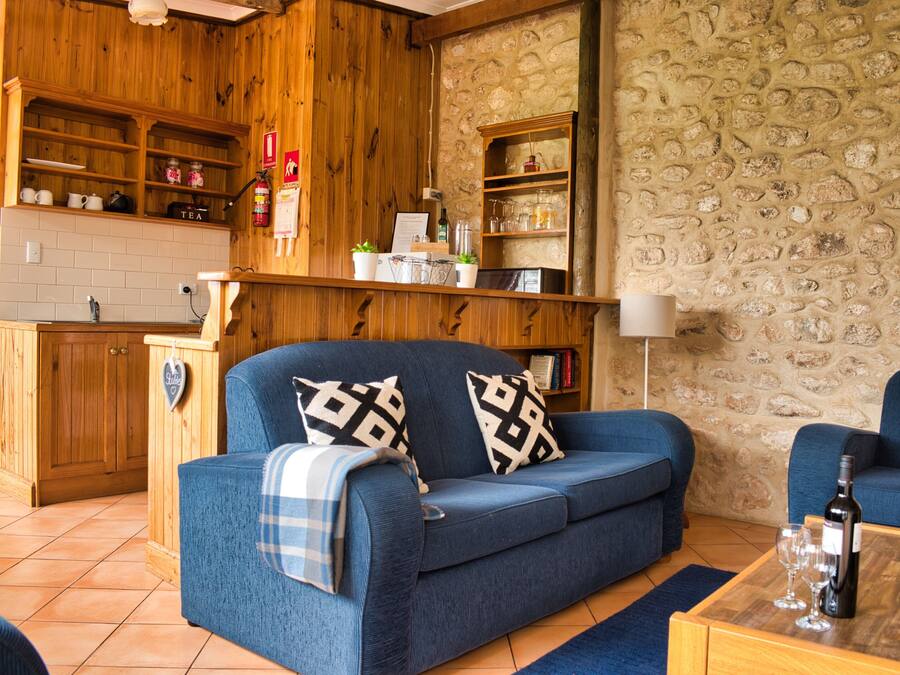 Un accogliente soggiorno con un divano blu, mensole in legno, un muro in pietra e un angolo cottura.