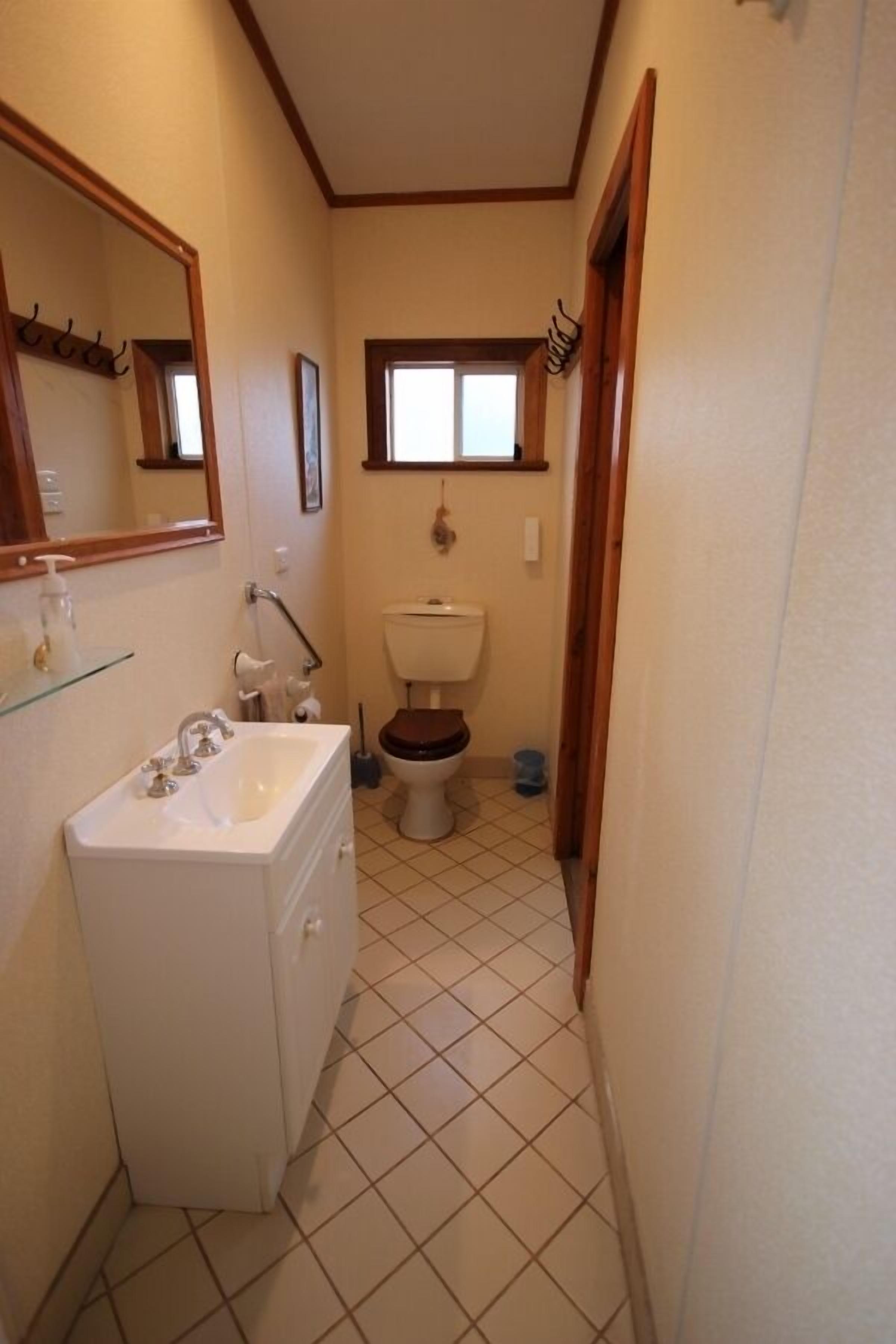 Un baño estrecho con un lavamanos blanco, un inodoro y una ventana sobre el inodoro.
