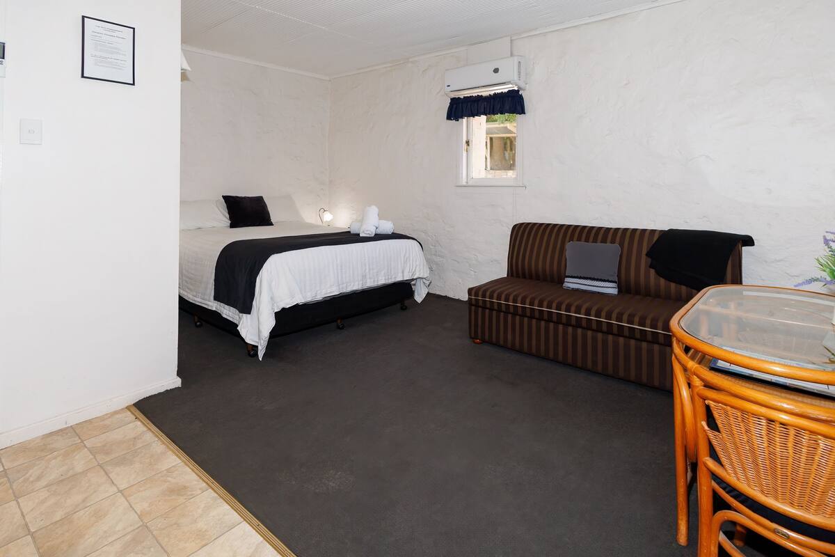 Une chambre d’hôtel avec un lit, un canapé, une petite table et une fenêtre avec un rideau.