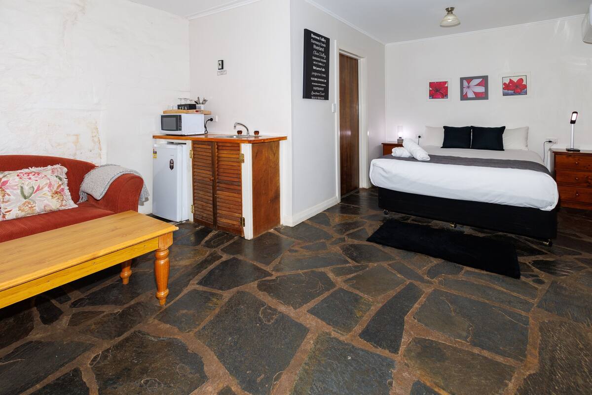 Une pièce comprenant un lit, une petite kitchenette, une table en bois et un canapé rouge.