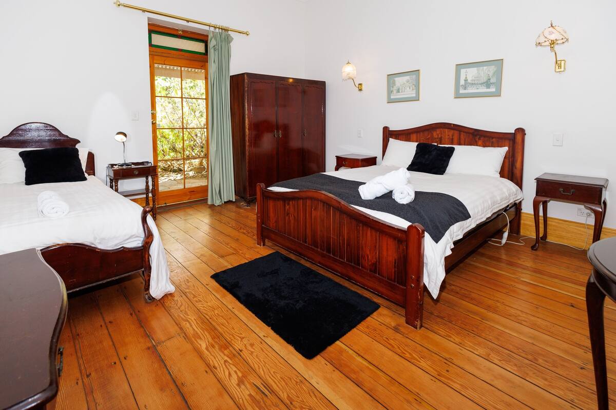Une chambre d’hôtel avec deux lits en bois, une armoire, une petite table et un tapis noir.