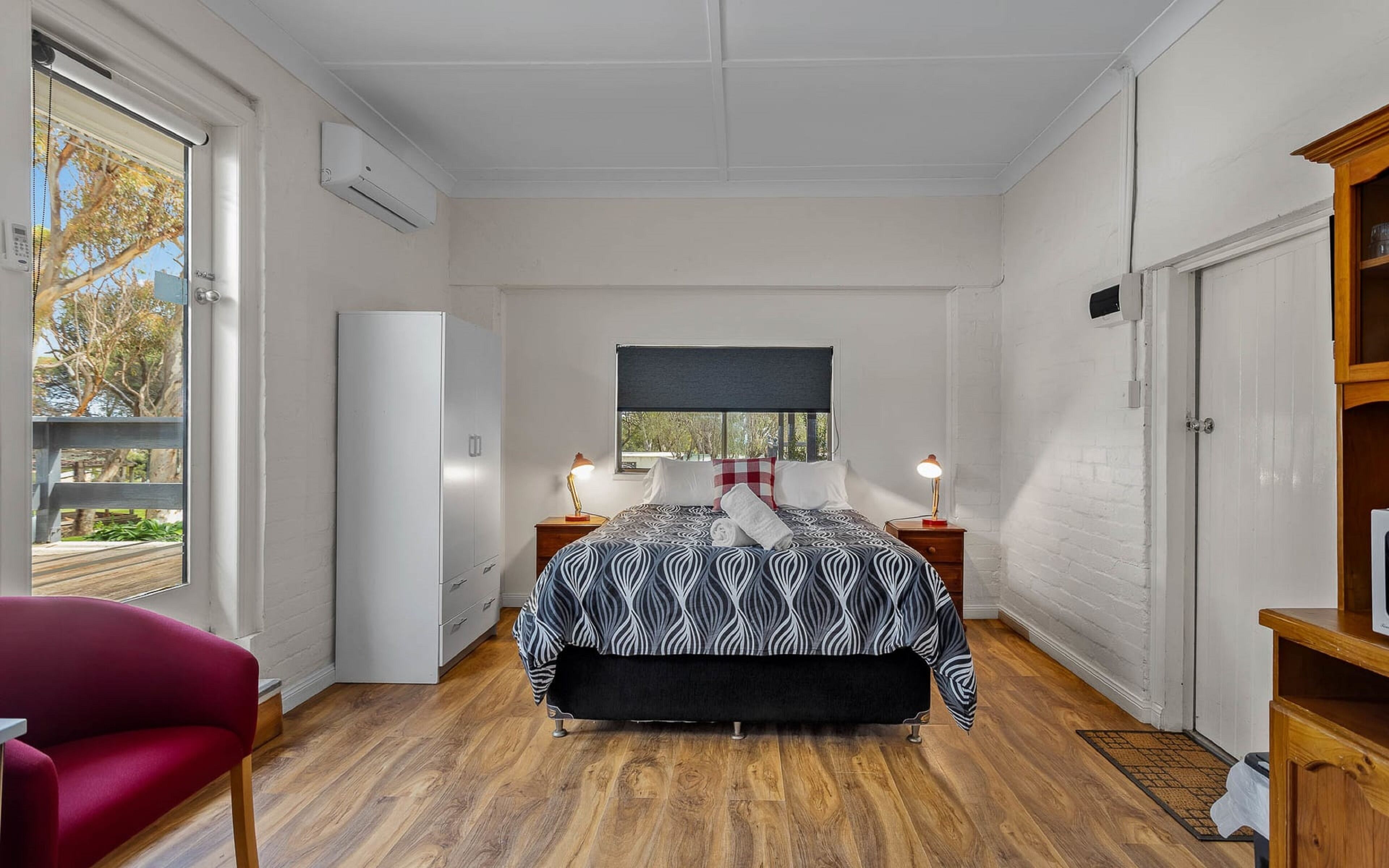 Una camera da letto con un letto, comodini, un armadio, una sedia rossa e vista sull'esterno.