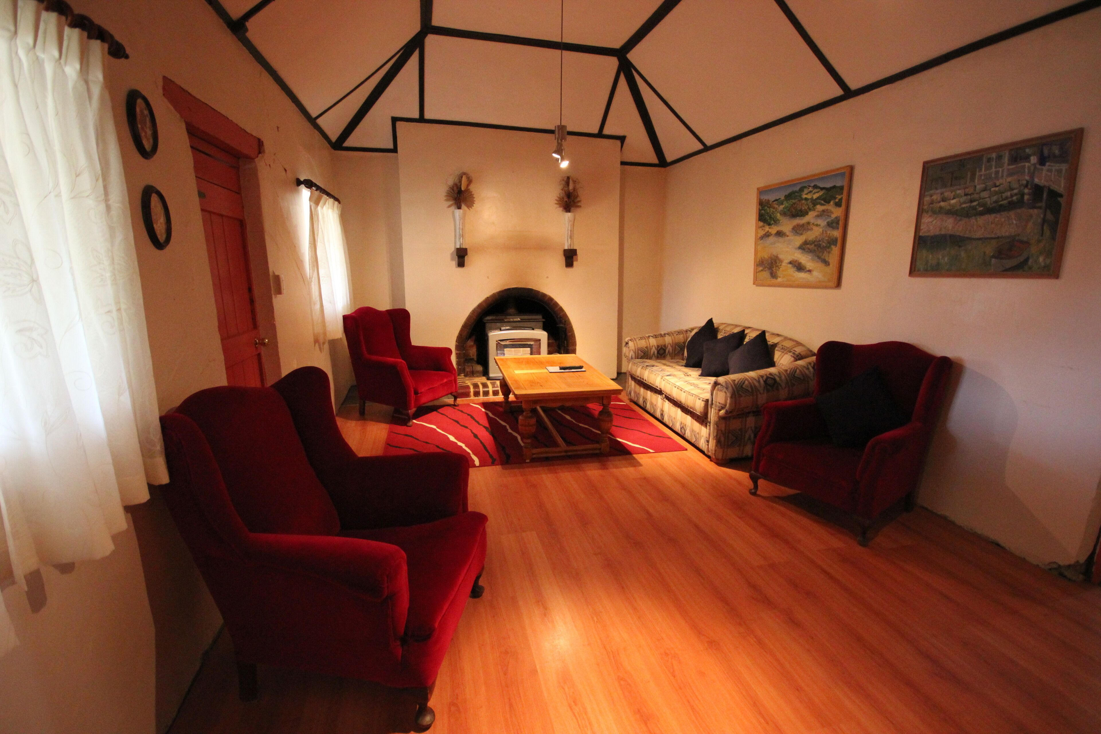 Un salon avec une cheminée, des fauteuils rouges, un canapé et un plancher en bois.
