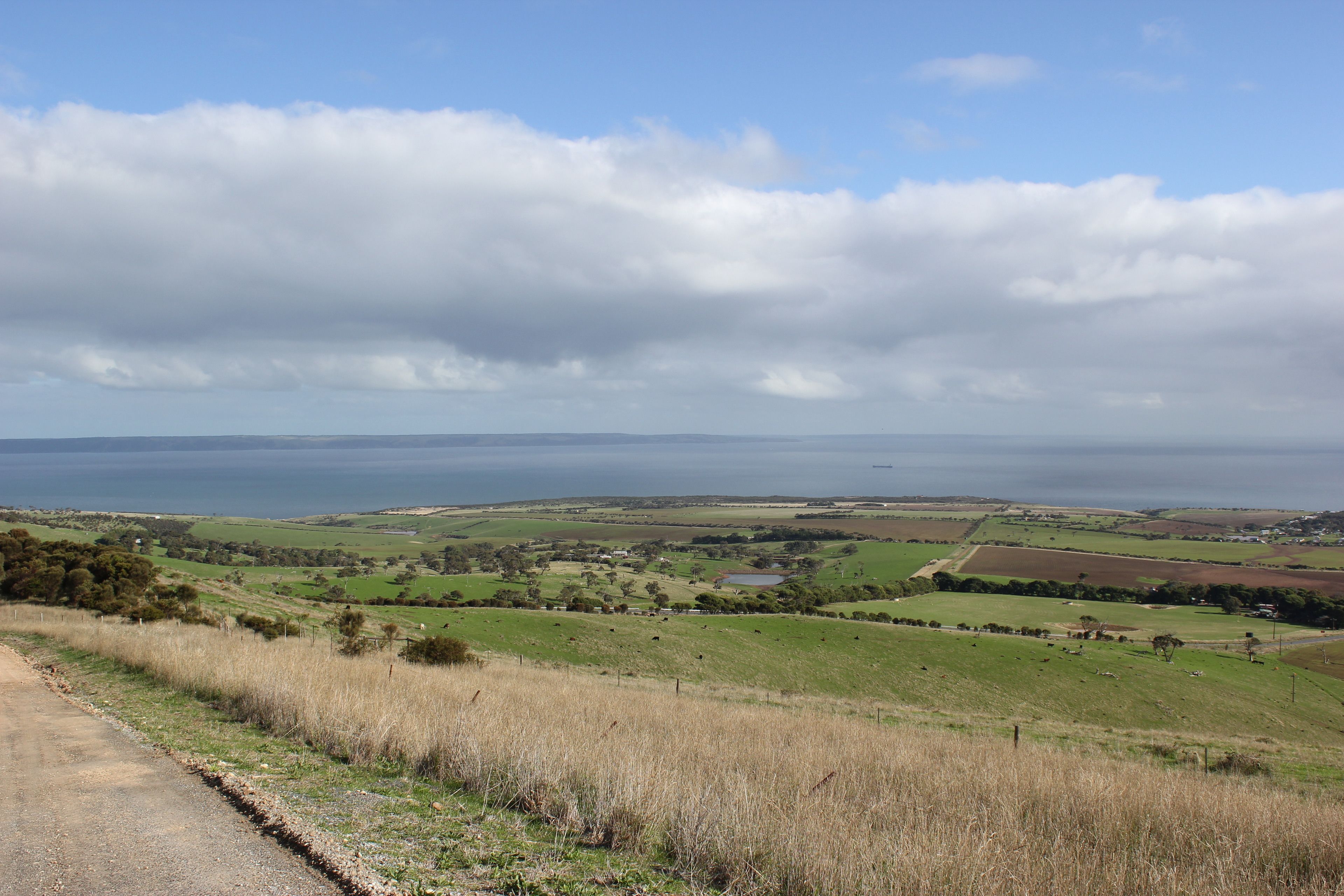 A rural landscape with a road, fields, and a body of water in the distance.