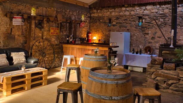 Un intérieur rustique avec un mur en pierre, des sièges en forme de tonneaux en bois, un coin bar et une cheminée.